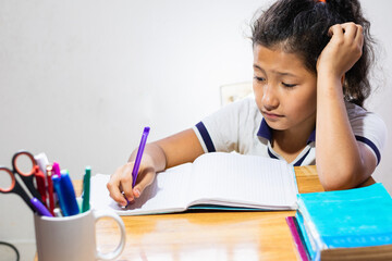latina brunette student, very bored and stressed out doing her homework. little girl writing on her wooden desk
