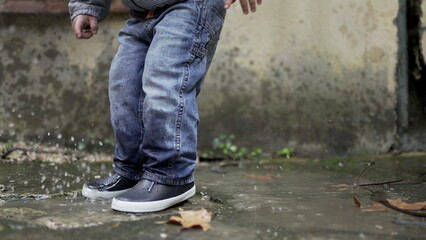 Toddler boy splashes into puddle of water. Child plays with puddles