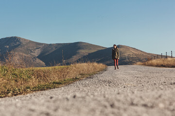 A girl walks along a rural road against the backdrop of mountains.