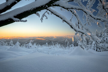 Yellow glow on a distant horizon above Little Fatra mountains on a cold day of winter with lots of snow. Vast forests covered in frost and snow. Beautiful winter day in the mountains.