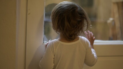 Fototapeta na wymiar Toddler child staring outside standing by window at home