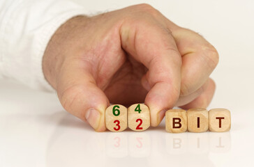 On the reflective surface in the hands of a man are cubes with the inscription - 64 bit or 32 bit