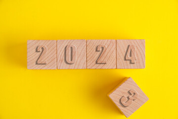 Wooden cubes with numbers 2023 yellow background turning into 2024.