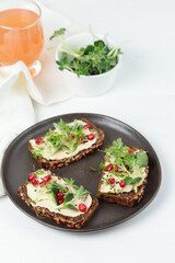 Superfood Sandwiches with soft cheese, microgreens, pomegranate seeds. Close-up on a white background, a glass of juice in the background.