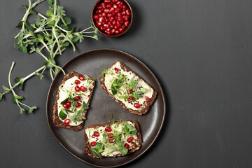 Sandwiches with soft cheese, microgreens, pomegranate seeds. Close-up on a black background, a glass of juice in the background.