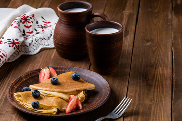 Obraz na płótnie Canvas Pancakes with strawberries and blueberries, jug with milk, ceramic dishes in the style of rustic