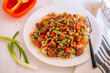 Vegan, plant based version of  US Southern Hoppin John with black eyed peas, brown rice, red bell pepper, spring green onions in a white plate