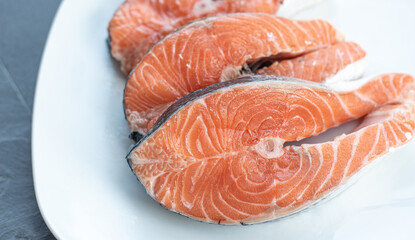 Close up of three fresh salmon slices, in a white plate, on a slate table..Tasty food from Italian cuisine and from the Mediterranean sea. Concept for a tasty and healthy meal.
