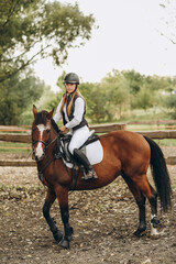 A young female jockey is sitting on her horse in show jumping training. Preparing for the...