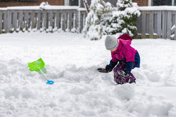 Little child playing with snow and showel outdoors near house in winter. Wintertime fun outdoor activities for children.