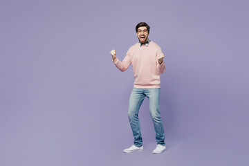 Full body young caucasian IT man he wears casual clothes pink sweater glasses doing winner gesture celebrate clenching fists say yes isolated on plain pastel light purple background studio portrait.