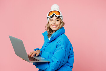 Sise view snowboarder IT woman in blue suit goggles mask hat ski padded jacket work hold use laptop pc computer isolated on plain pastel pink background Winter extreme sport hobby trip relax concept © ViDi Studio