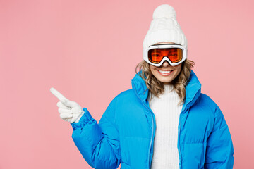 Snowboarder woman 20s wear blue suit goggles mask hat ski padded jacket point index finger aside on area isolated on plain pastel pink background Winter extreme sport hobby weekend trip relax concept