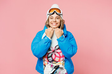 Snowboarder smiling woman wear blue suit goggles mask hat ski padded jacket hold snowboard look camera isolated on plain pastel pink background. Winter extreme sport hobby weekend trip relax concept.