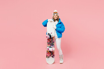 Full body snowboarder smiling woman wears blue suit goggles mask hat ski padded jacket hold snowboard isolated on plain pastel pink background. Winter extreme sport hobby weekend trip relax concept.