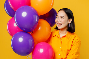 Fototapeta na wymiar Close up happy fun smiling young woman wearing casual clothes celebrating holding looking at bunch of colorful air balloons isolated on plain yellow background. Birthday 8 14 holiday party concept.