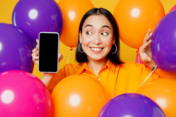 Close up fun young woman wearing casual clothes celebrating in bunch of balloons use mobile cell...