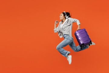 Traveler woman of African American ethnicity wear casual clothes hold bag run isolated on plain orange background Tourist travel abroad in free spare time rest getaway Air flight trip journey concept