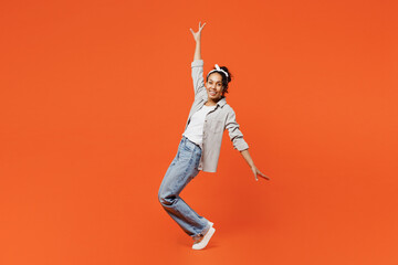 Full body young woman of African American ethnicity she wear grey shirt headband stand on toes leaning back with outstretched hands isolated on plain orange background studio People lifestyle concept
