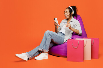 Full body fun young woman wears grey shirt sit in bag chair using mobile cell phone hold credit...