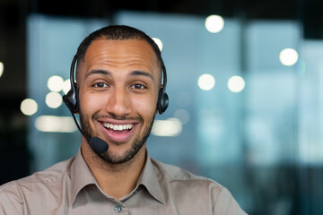 Close up hispanic male worker with video headset smiling and looking at camera, tech support worker...