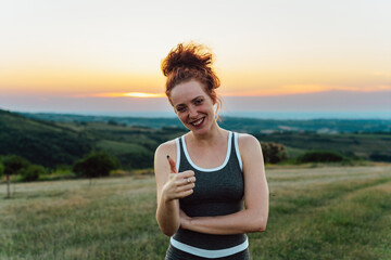 Portrait of smiling red hair sporty woman in sporty outfit, she holding thumbs up.