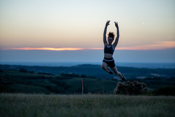 Silhouette of young woman jumping against sunset