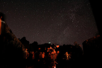 Mountains at night and stars in the sky, shooting stars and planets in the sky. Noisy photo at long exposure. People look at the stars through a telescope, stargazing