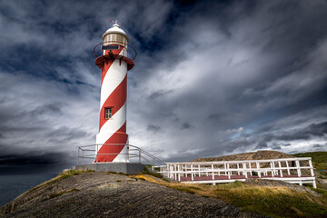 Red and white striped lighthouse with a solar panel under a stormy sky near Heart's Content...