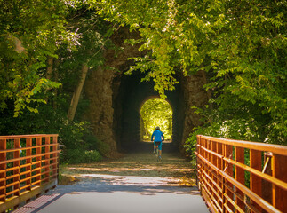 View of  the tunnel on Midwestern recreational trail in summer; male bicyclists in blue jersey in the distance