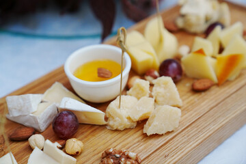 wooden tray with cheese cuts, nuts, grapes and honey. 