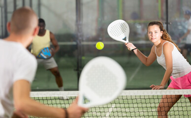 Young beautiful woman in white t-shirt playing padel tennis indoor