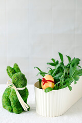 Colorful egg with a ribbon in a pot next to the green grass, next to the figure of a rabbit