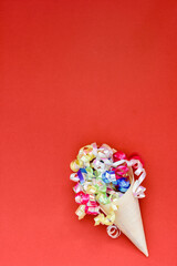 Paper cone with colorful party streamers on red background.