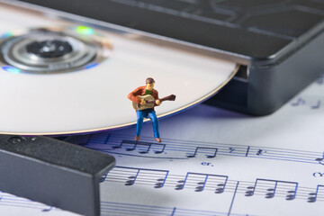 a white cd in a cd player, lying on a sheet of music on which a musician plays the guitar.