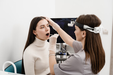 Otolaryngologist examines woman throat with spatula. Consultation with laryngologist. ENT doctor doing oropharyngoscopy procedure.