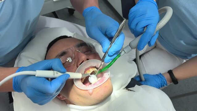 teeth cleaning middle-aged man plaque calculus in mouth lip and cheek retractor doctors 4 hands cleaning teeth suction plaque on teeth visible teeth gums treatment dental office latest technology