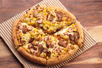 Freshly baked american pan pizza with a lot of cheese, chicken sausage, thin and crispy kebab meat and corn on a wooden board, take-away dish