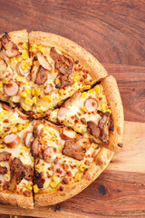 Freshly baked american pan pizza with a lot of cheese, chicken sausage, thin and crispy kebab meat and corn on a wooden board, take-away dish, top view