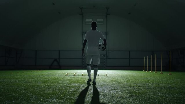 calm athlet with soccer ball walking in gym in night, slow motion rear view, future champion
