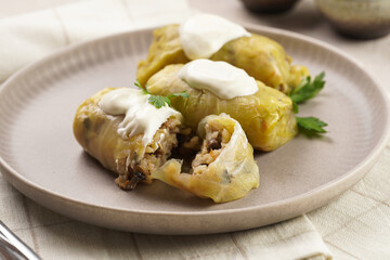 Three vegetarian cabbage rolls stuffed with rice, mushrooms, carrots and onions topped with vegan sour cream - traditional ukrainian dish during religious fasting time periods - on a grey plate