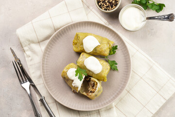 Three vegetarian cabbage rolls stuffed with rice, mushrooms, carrots and onions topped with vegan sour cream, traditional ukrainian dish during religious fasting time periods on a grey plate, top view