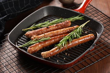 Traditional german organic pork sausages grilled on a red grill pan with rosemary branches and whole black pepper seeds on a baking rack on a wooden background