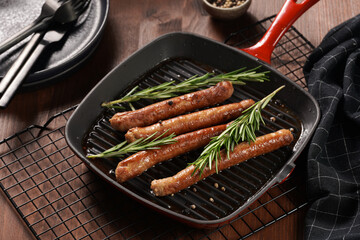 Traditional german organic pork sausages grilled on a red grill pan with rosemary branches and whole black pepper seeds on a baking rack on a wooden background