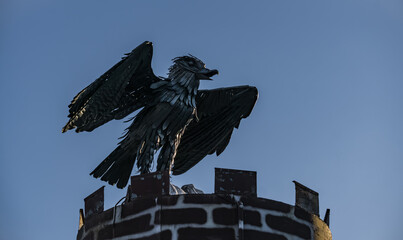 Metal figurine sculpture of a mountain eagle on a pedestal against the blue sky, decorative figurine of a bird