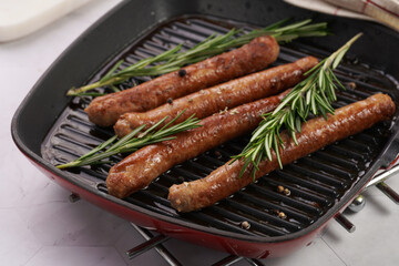 Traditional german organic pork sausages grilled on a red grill pan with rosemary branches and whole black pepper seeds on a marble background