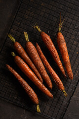 roasted young carrots with greens on a black baking rack on a brown background