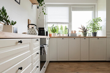 Fototapeta na wymiar Modern kitchen with kitchen furniture with white cabinets and drawers. Wooden countertop and plants in stylish interior of kitchen. 