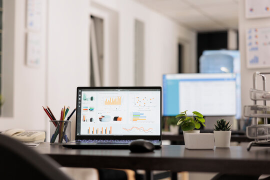 Management workstation with laptop computer displaying statistical data of the company financial results. Empty office during staff break time, indoor workplace concept.