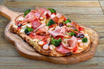 Pizza with salami, ham, vienna sausages, kalamata, olives, broccoli, pelati, pesto. Roman pizza rectangular on wood background